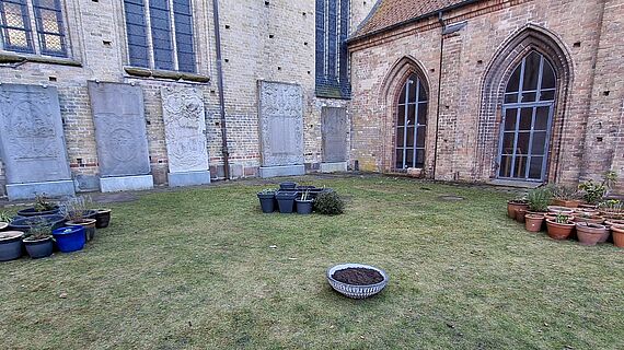 Auf einer Rasenfläche in Innenhof des Kreuzganges stehen in Gruppen Pflanztöpfe in verschiedenen Farben.