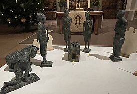 verschiedene Krippenfiguren aus Bronze sind auf einer weißen Fläche aufgestellt. 