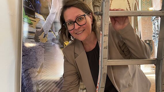 Eine Frau steht auf einer Leiter im Schleswiger Dom. Die Frau ist zur Hälfte und von vorne zu sehen. 