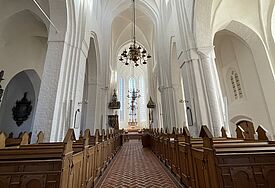 Kircheninneraum im Stil der Gotik mit weißen Säulen, im Hintergrund die hellen Chorfenster
