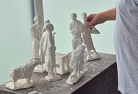 Ein Mann fasst eine Krippenfigur aus Gips an. Sie steht mit anderen Figuren auf einem Podest.