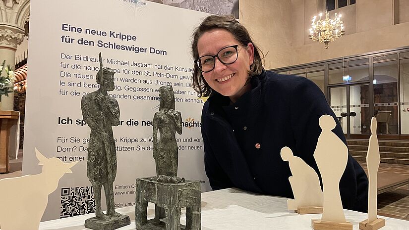 Eine Frau beugt sich über die Krippenfiguren Maria, Josef und dem Jesuskind