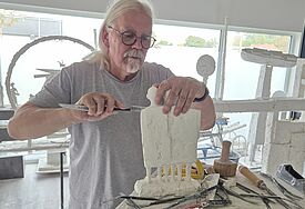 Ein Künstler arbeitet mit Werkzeugen an einer Gruppe von kleinen Figuren aus Gips